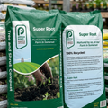 Two bags of Pennys Super Root compost on a wooden pallet with a garden setting in the background.