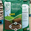 Two bags of Nutri Boost compost with a green field graphic on a blurred indoor background.
