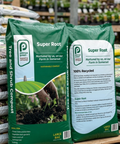 Two bags of Pennys Super Root compost on a wooden pallet with a garden setting in the background.