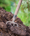 Rake on a pile of compost with greenery in the background