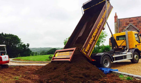 Dump truck unloading soil onto a construction site with a building in the background.